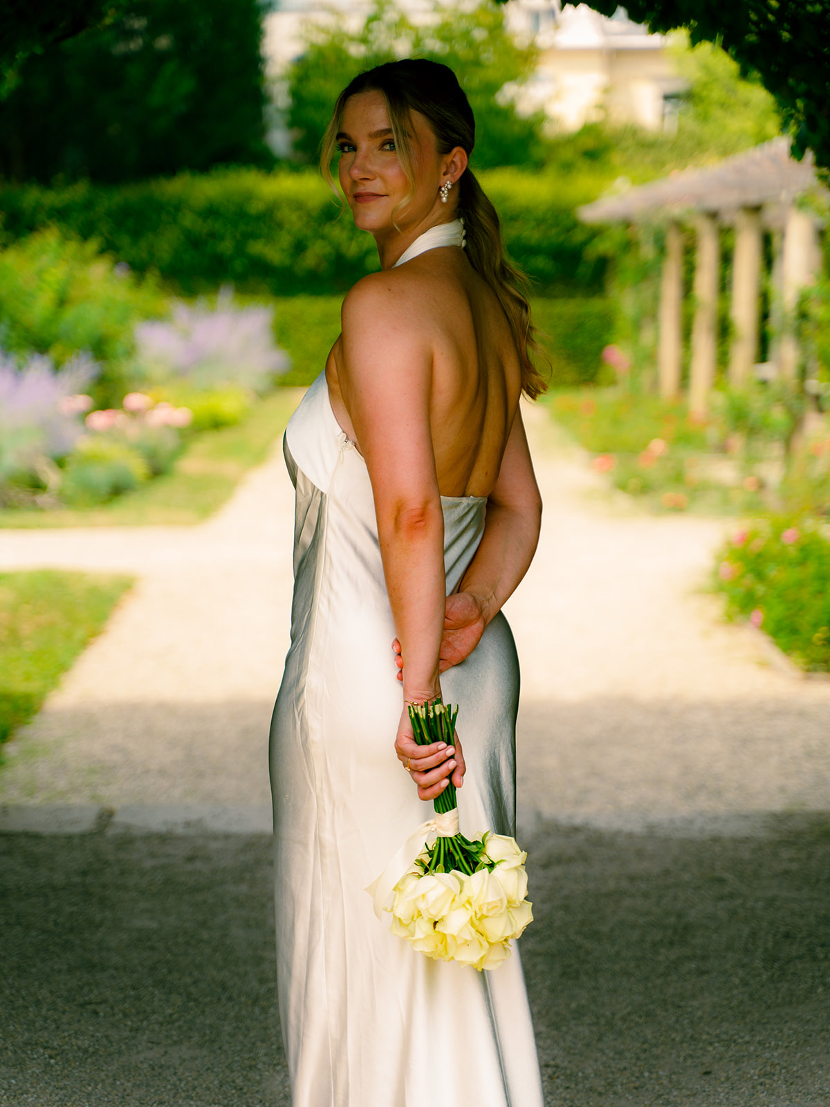 Braut im Seidenkleid mit Rosenstrauß im Garten